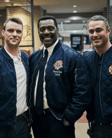 a man in a battalion chief jacket poses for a photo with two other men