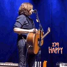 a man singing into a microphone while holding a guitar with the words " i 'm happy " behind him