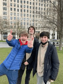 three young men are standing next to each other and giving a thumbs up .