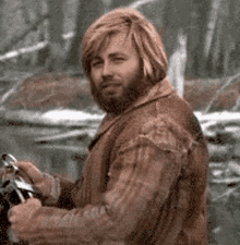 a man with a beard and long hair is holding a steering wheel of a motorcycle .