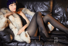 a woman wearing a fur coat and black tights sits on a black leather couch