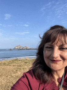 a woman in a red shirt smiles in front of a beach