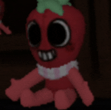 a stuffed strawberry with big eyes and a green leaf on top is sitting in a dark room .