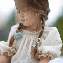 a little girl with braids is wearing a white dress with polka dots and a blue flower .