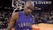 a man in a toronto raptors jersey is standing on a basketball court with a crowd in the background .