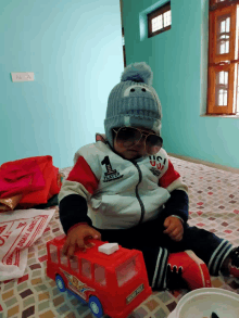 a baby wearing a hat and sunglasses is playing with a red toy bus