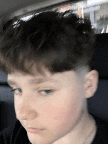 a young boy with a shaved head sits in a car with his eyes closed