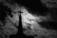 a black and white photo of a church steeple with a cross on top of it against a cloudy sky .