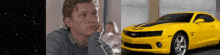 a man sitting next to a yellow car that says camaro on it