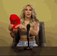 a woman is sitting in front of a microphone holding a red hat that says ' yst ' on it .