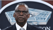 a man in a suit and tie stands in front of the pentagon logo