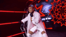 a man in a white coat and shorts is standing in a ring with red lights behind him .