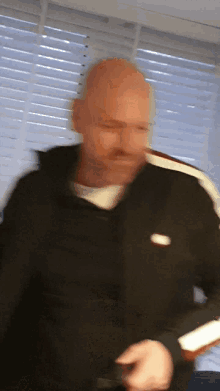 a bald man wearing a black nike jacket looks at something