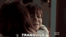 a woman hugging another woman with tranquila written on the bottom right