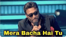 a man wearing sunglasses and a suit is holding a microphone and saying `` mera bacha hai tu '' .