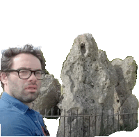 a man wearing glasses stands in front of a rock