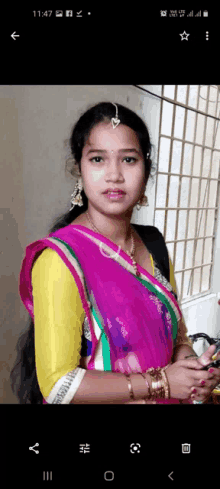 a woman wearing a pink saree and a yellow shirt is standing in front of a window .