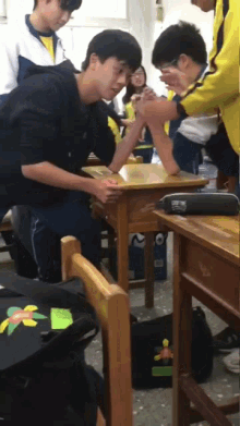 a group of boys arm wrestling in a classroom with a pencil case that says ' a ' on it