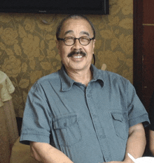 a man wearing glasses and a blue shirt is smiling in front of a panasonic television