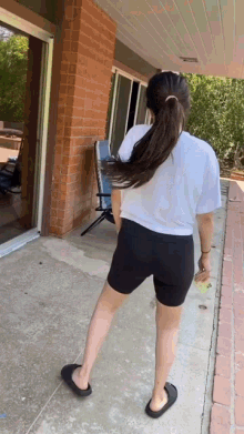 a woman in a white shirt and black shorts is standing on a sidewalk in front of a brick building