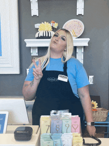 a woman in a blue shirt and black apron stands behind a counter in front of a display of numbered candles