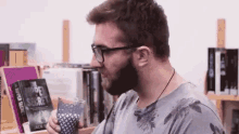 a man with a beard and glasses is sitting in front of a bookshelf holding a glass of water .