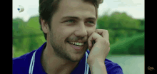 a man in a blue shirt is smiling and talking on a phone