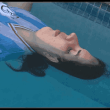 a woman in a blue and white shirt is floating in a swimming pool