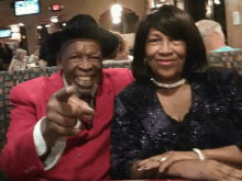 a man in a red suit is pointing at the camera while sitting next to a woman