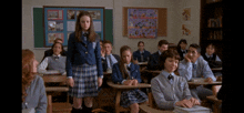 a girl in a plaid skirt stands in front of a classroom full of people