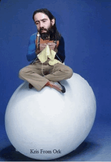 a man with a beard is sitting on top of an egg knitting