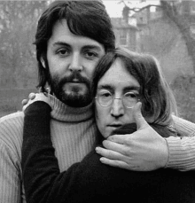 a black and white photo of a man with a beard and glasses hugging a woman .