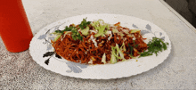 a white plate topped with noodles and vegetables next to an orange bottle of ketchup