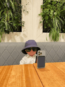 a baby wearing sunglasses and a purple hat sits at a table