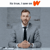 a man in a suit and tie is sitting at a desk with his hands folded in front of an orange w logo