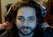 a man with long hair and a beard looks at the camera in front of a typewriter