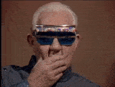 a man wearing a pair of blue sunglasses covering his mouth with his hand