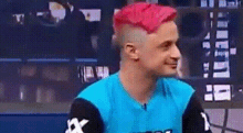 a man with pink hair and a mohawk is wearing a blue shirt and black sleeves .