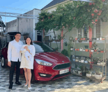 a man and woman standing in front of a red ford