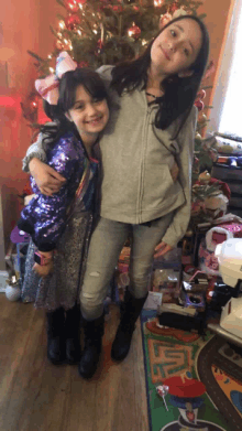 two girls standing in front of a christmas tree