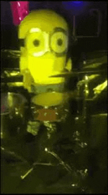 a yellow toy minion is playing drums in a dark room .