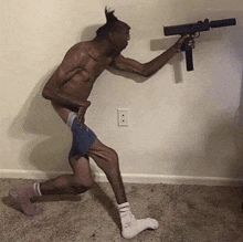 a shirtless man is holding a gun in a room while wearing socks .