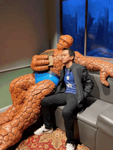 a man sits on a couch next to a statue of captain america