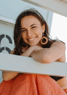 a woman wearing a headband and hoop earrings smiles while leaning on a railing