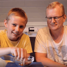 a man and a boy are sitting at a table with a bowl of food in front of them