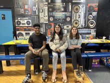 three people wearing roller skates are sitting on a bench in front of a wall with radios on it