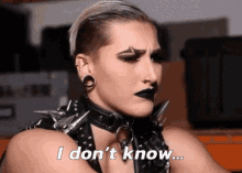 a woman with black makeup and spikes on her collar is saying i don 't know .