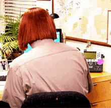 a woman with red hair is sitting at a desk with a telephone and a map on the wall behind her .