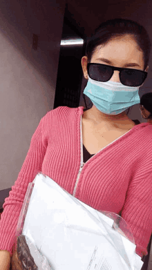 a woman wearing a pink sweater and a mask holds papers