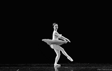 a black and white photo of a ballerina in a tutu standing on one leg on a black background .